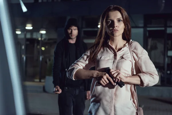 Femme avec arme regardant la caméra près du voleur la nuit — Photo de stock