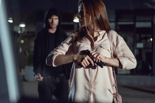 Mulher com arma perto de ladrão à noite — Fotografia de Stock