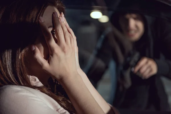 Ladrón apuntando arma a la mujer sentada en el coche por la noche - foto de stock