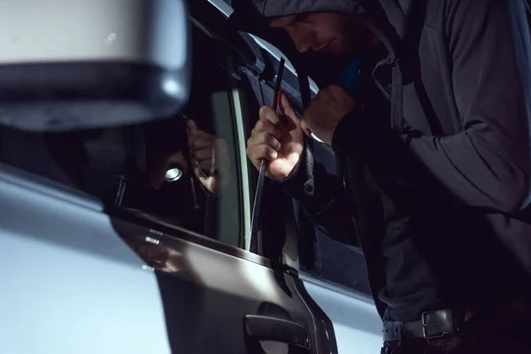 Thief intruding car with flashlight and crowbar — Stock Photo