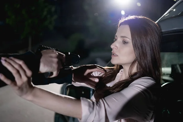 Злодій вказує пістолет на перелякану жінку, сидячи в машині вночі — стокове фото