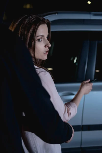 Ladrón atacando mujer por detrás cerca de coche por la noche - foto de stock
