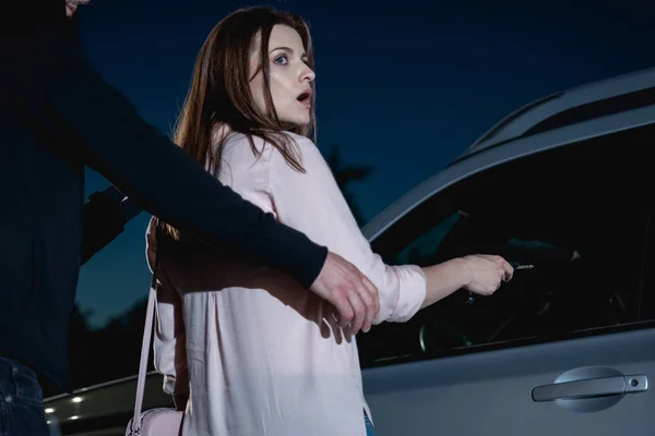 Ladrón atacando asustada mujer por detrás cerca de coche - foto de stock