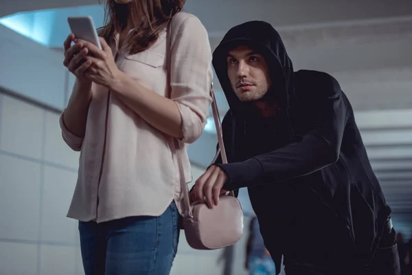 Ladrón robar dinero de la bolsa de la mujer usando el teléfono inteligente - foto de stock