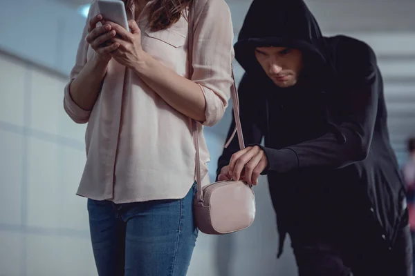 Ladrón robar dinero de la bolsa de la mujer usando el teléfono inteligente - foto de stock