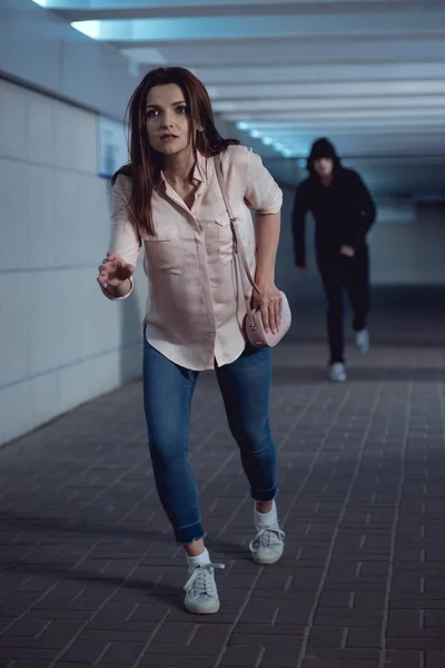 Mujer asustada huyendo de ladrón en el paso subterráneo - foto de stock