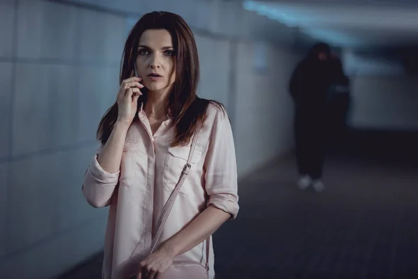 Enfoque selectivo de la mujer hablando en el teléfono inteligente cerca de ladrón en el paso subterráneo - foto de stock