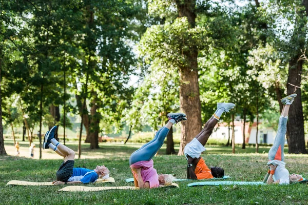 Homens e mulheres aposentados multiculturais que se exercitam em tapetes de fitness perto de árvores — Fotografia de Stock