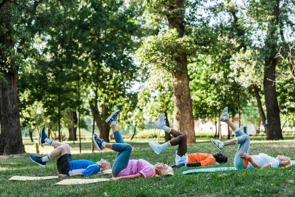 Hombres y mujeres mayores multiculturales que hacen ejercicio sobre colchonetas de fitness cerca de los árboles - foto de stock