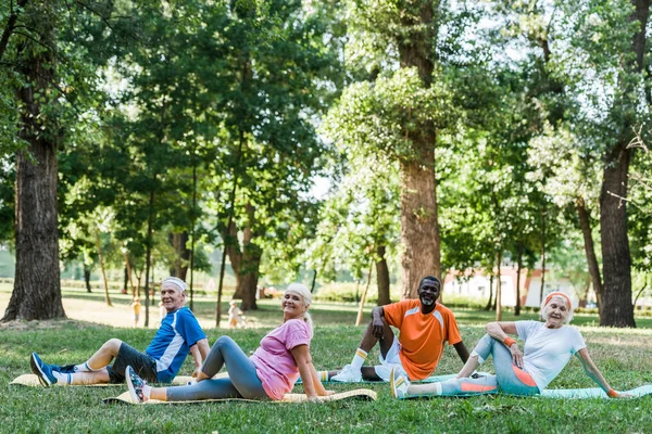 Happy senior women with grey hair and multicultural men sitting on fintess mats — Stock Photo