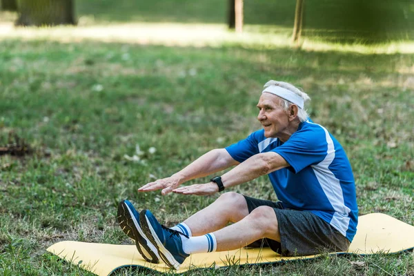 Felice pensionato esercizio sul tappeto fitness nel parco — Foto stock