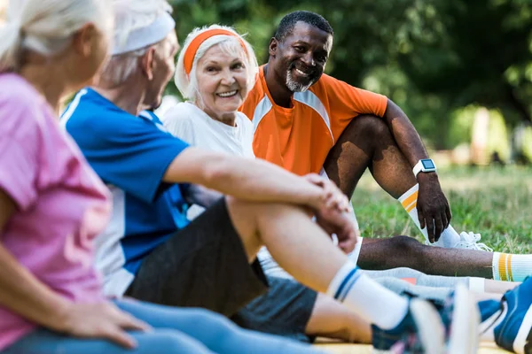 Foyer sélectif des hommes et des femmes multiculturels heureux en vêtements de sport assis sur des tapis de fitness — Photo de stock