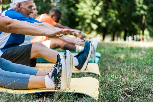 Cropped view of athletic retired and multicultural men and woman exercising on fitness mats — Stock Photo