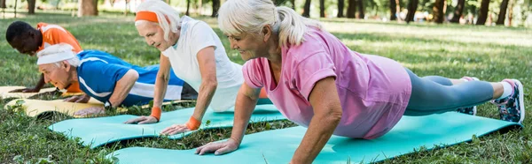 Panoramaaufnahme sportlicher Rentner und multikultureller Männer und Frauen in Sportbekleidung, die auf Fitnessmatten trainieren — Stockfoto