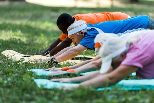 Selective focus of multicultural senior men and women stretching on fitness mats in park — Stock Photo