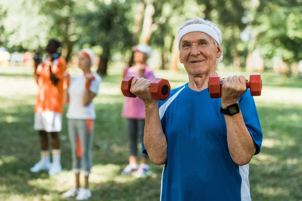 Selective focus of happy senior man holding dumbbells in park — Stock Photo