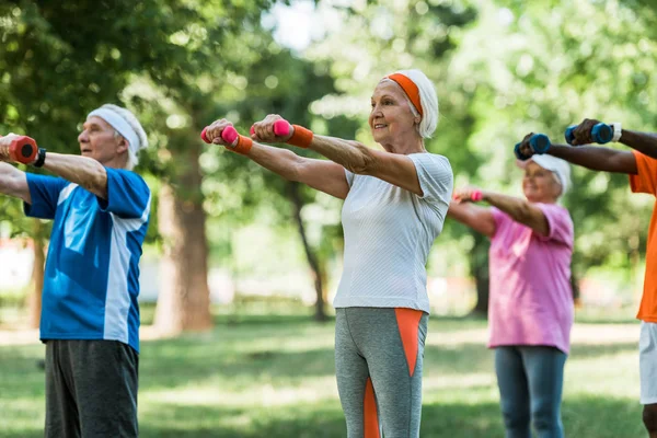 Enfoque selectivo de los pensionistas senior que ejercen con pesas en el parque - foto de stock