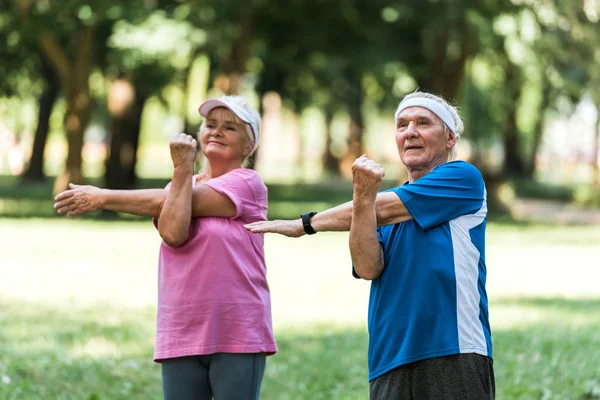 Happy retired couple doing exercises while standing in park — Stock Photo