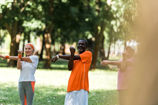 Selective focus of happy milticultural retired women and man working out in park — Stock Photo