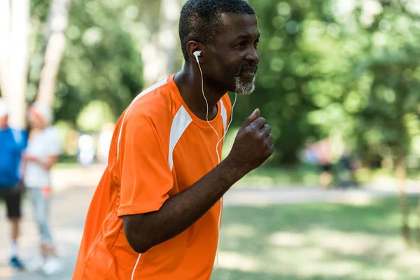 Enfoque selectivo del hombre afroamericano retirado corriendo y escuchando música en auriculares - foto de stock
