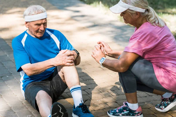 Anziana donna in berretto seduta vicino a pensionato uomo toccare ginocchio — Foto stock