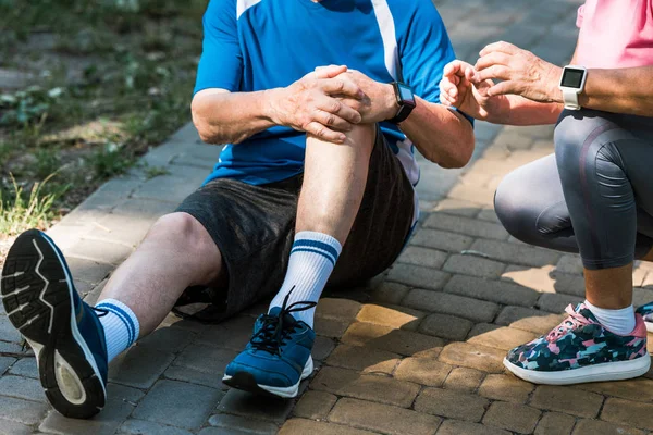 Vista ritagliata della donna anziana seduta vicino all'uomo in pensione toccare il ginocchio — Foto stock