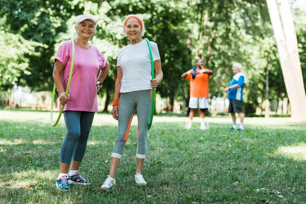 Selective focus of cheerful senior women smiling while holding hula hoops near multicultural retired men — Stock Photo