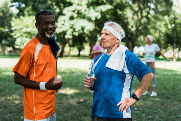 Foco seletivo de esportivos multiculturais homens seniores segurando garrafas com água — Fotografia de Stock