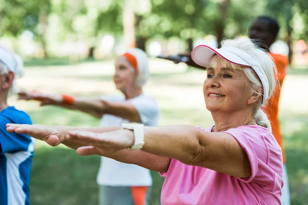 Enfoque selectivo de la mujer jubilada haciendo ejercicio cerca de pensionistas multiculturales en el parque - foto de stock