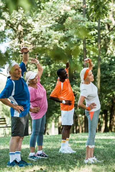 Foyer sélectif des hommes et des femmes âgés multiculturels joyeux debout avec les mains sur les hanches tout en faisant de l'exercice — Photo de stock