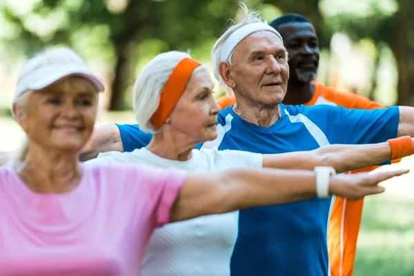 Enfoque selectivo de hombre jubilado feliz de pie con las manos extendidas cerca de los pensionistas multiculturales - foto de stock