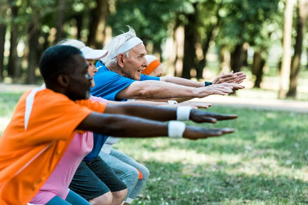 Selective focus of cheerful retired man with outstretched hands near multicultural pensioners — Stock Photo
