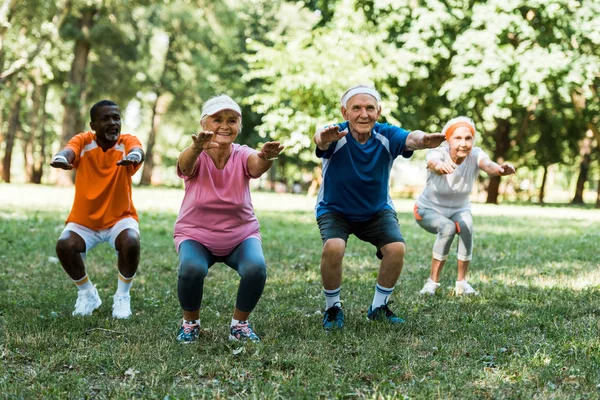 Pensionistas multiculturales haciendo sentadas en el parque sobre hierba verde - foto de stock