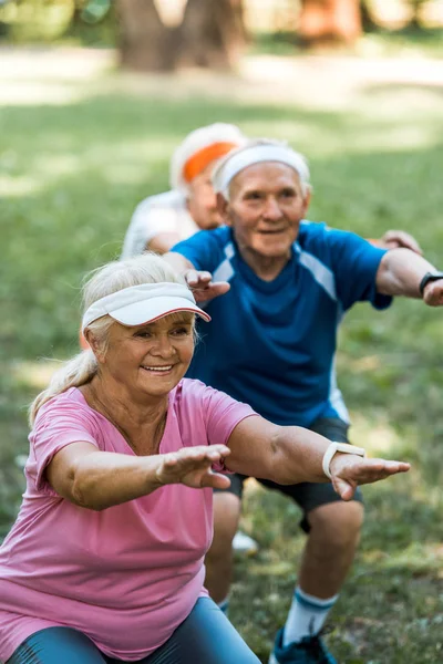 Enfoque selectivo de personas jubiladas multiculturales felices haciendo sentadas en la hierba - foto de stock