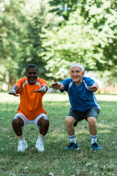 Alegre retirado y multicultural med haciendo sit ups en hierba - foto de stock