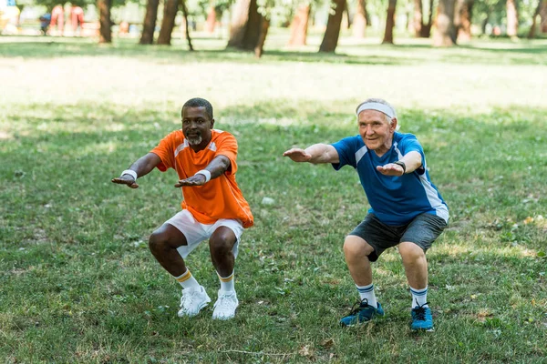 Счастливый пенсионер и мультикультурный медик делает приседания на траве — стоковое фото