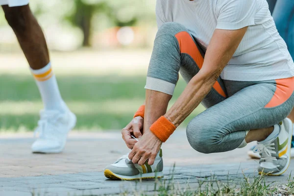 Cropped view of senior woman sitting and tying shoelaces in park — Stock Photo