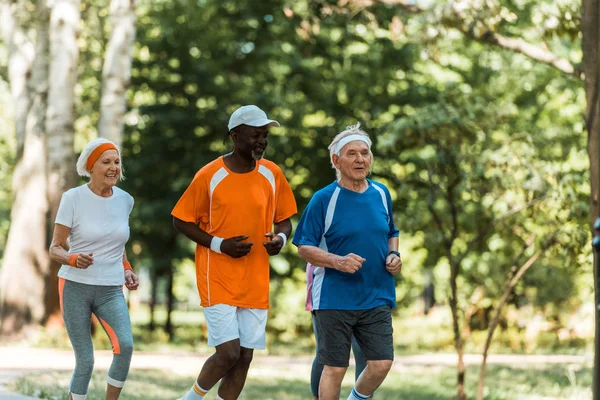 Hombres mayores multiculturales felices y mujer jubilada corriendo en el parque - foto de stock