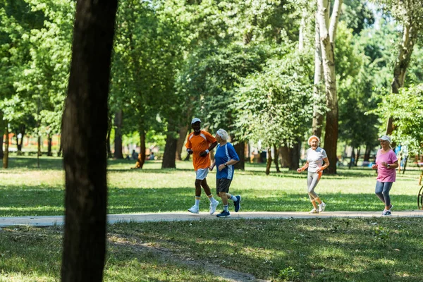 Selective focus multicultural and senior men and women in sportswear jogging in park — Stock Photo