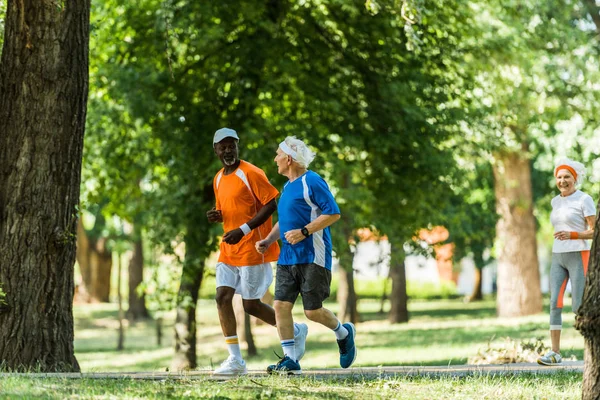 Enfoque selectivo de los hombres multiculturales felices corriendo con la mujer jubilada - foto de stock