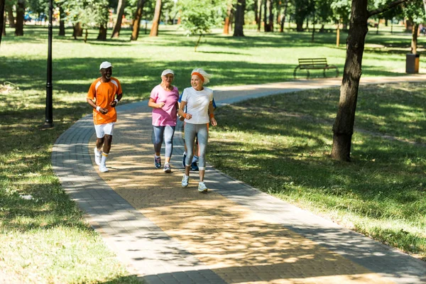 Glückliche Rentnerinnen laufen mit afrikanisch-amerikanischem Mann auf Gehweg — Stockfoto