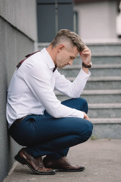 Seitenansicht eines aufgebrachten Geschäftsmannes in formeller Kleidung, der den Kopf berührt, während er draußen sitzt — Stockfoto