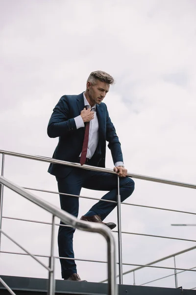 Foco seletivo de empresário chateado em terno de pé fora e tocar gravata — Fotografia de Stock