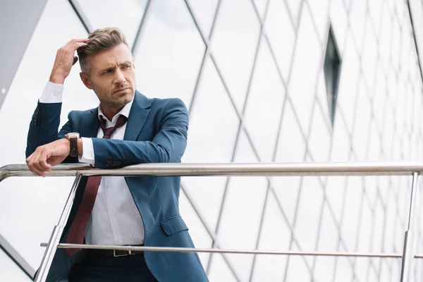 Vista de ángulo bajo del hombre de negocios pensativo en desgaste formal de pie afuera cerca del edificio - foto de stock