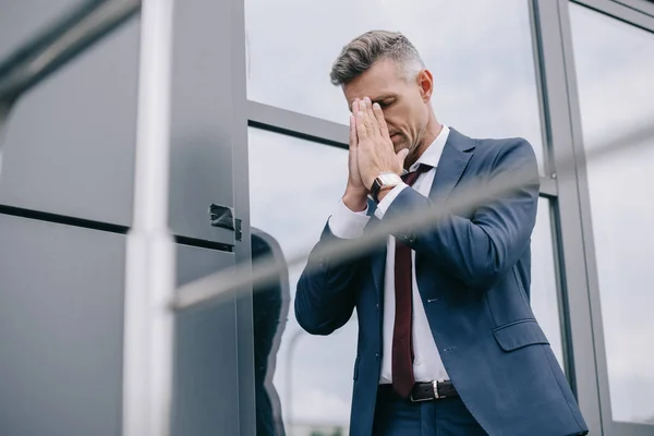 Selective focus of upset man in formal wear standing with praying hands near building — Stock Photo