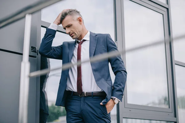 Selective focus of upset man in formal wear standing near building with hand in pocket — Stock Photo