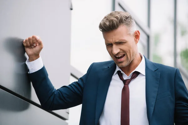 Emotional businessman in formal wear standing near building — Stock Photo