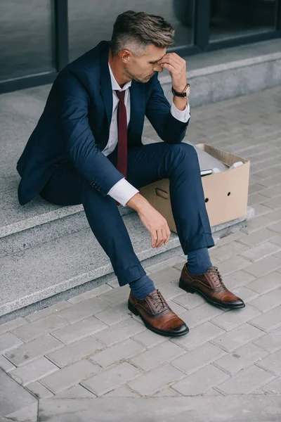 Bouleversé et licencié homme d'affaires assis sur les escaliers et toucher le visage — Photo de stock