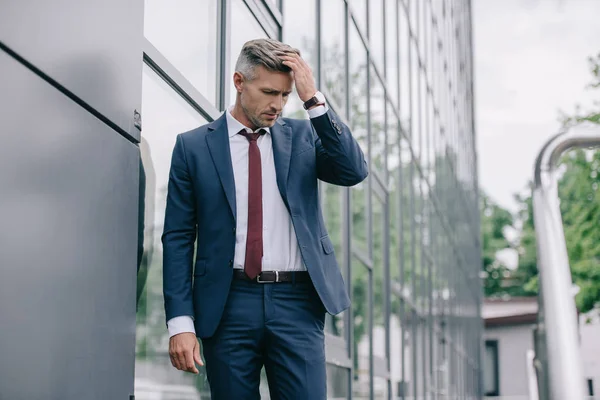 Selective focus of upset businessman in formal wear standing near building and touching hair — Stock Photo