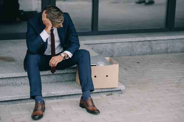 Homem de negócios demitido sentado nas escadas perto da caixa de papelão — Fotografia de Stock